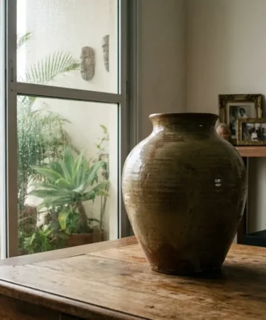 Sala com vaso artesanal em destaque e varanda úmida ao fundo